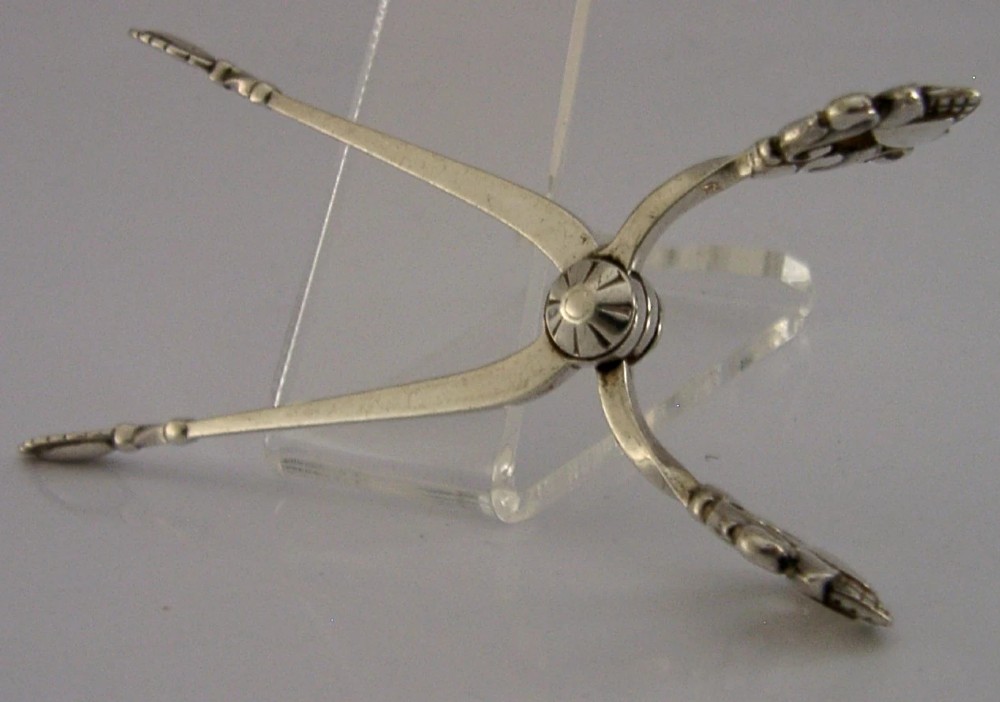 A pair of 1958 Georg Jensen sterling silver sugar tongs featuring the Acorn pattern handle design with central pivot joint and shell grips. View IV