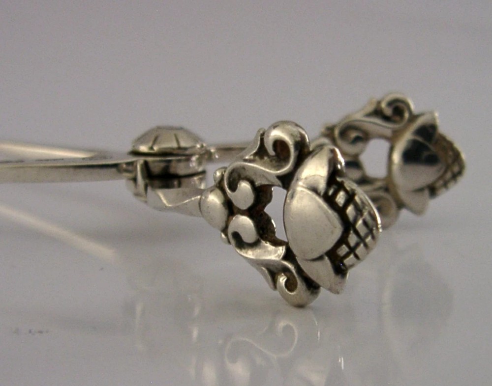 A pair of 1958 Georg Jensen sterling silver sugar tongs featuring the Acorn pattern handle design with central pivot joint and shell grips. View V