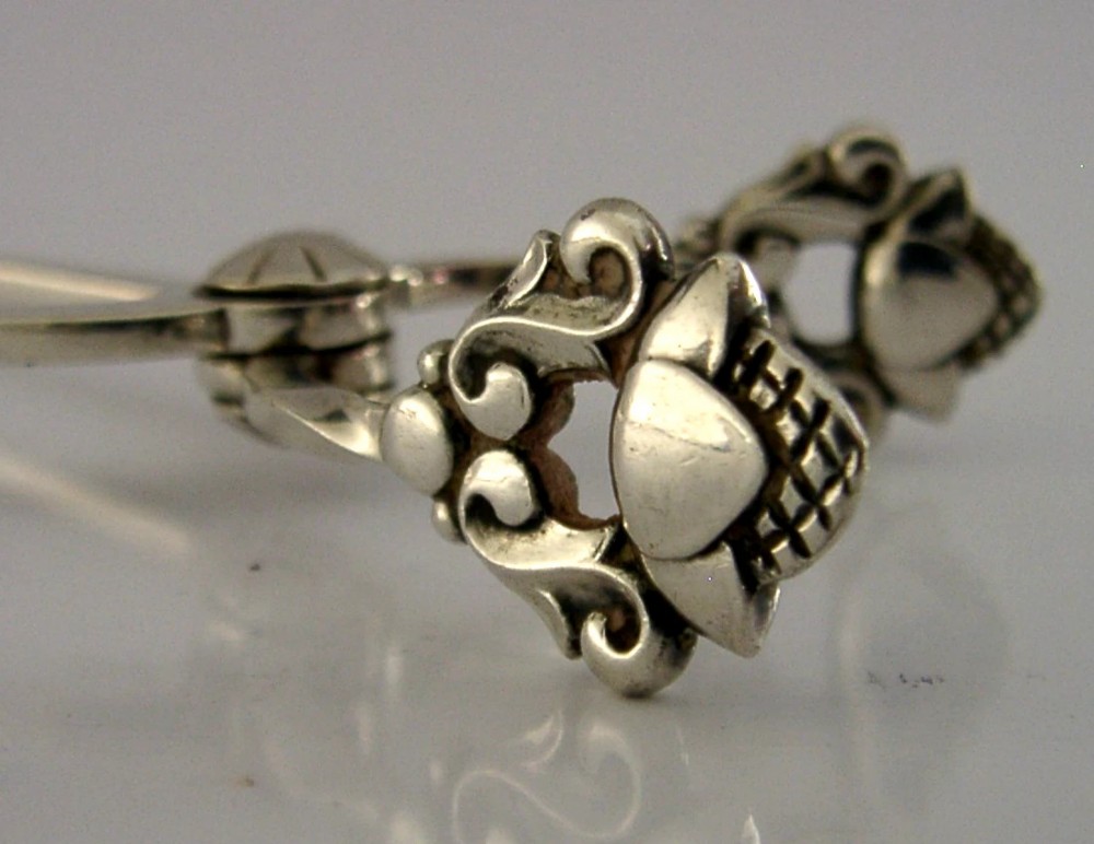 A pair of 1958 Georg Jensen sterling silver sugar tongs featuring the Acorn pattern handle design with central pivot joint and shell grips. View VI