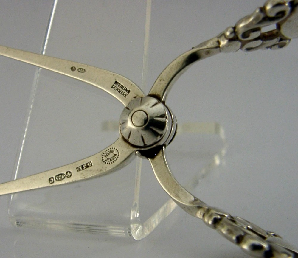 A pair of 1958 Georg Jensen sterling silver sugar tongs featuring the Acorn pattern handle design with central pivot joint and shell grips. View VII