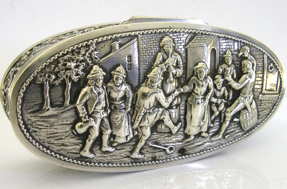An oval solid silver desk box decorated with high-relief repousse relief depicting traditional Dutch tavern dancers and musicians.