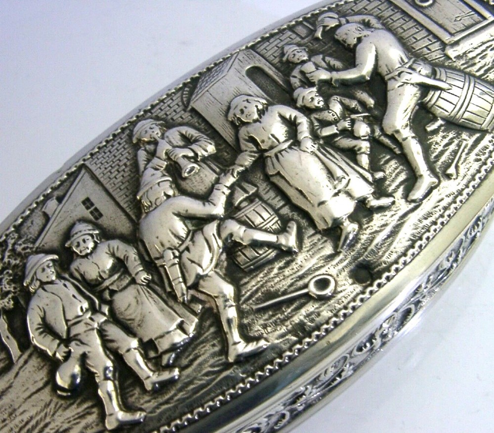An oval solid silver desk box decorated with high-relief repousse relief depicting traditional Dutch tavern dancers and musicians. View II