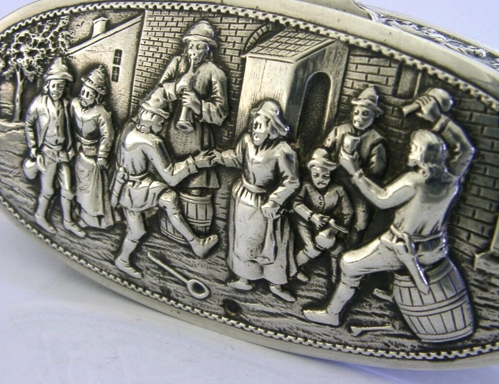 An oval solid silver desk box decorated with high-relief repousse relief depicting traditional Dutch tavern dancers and musicians. View V