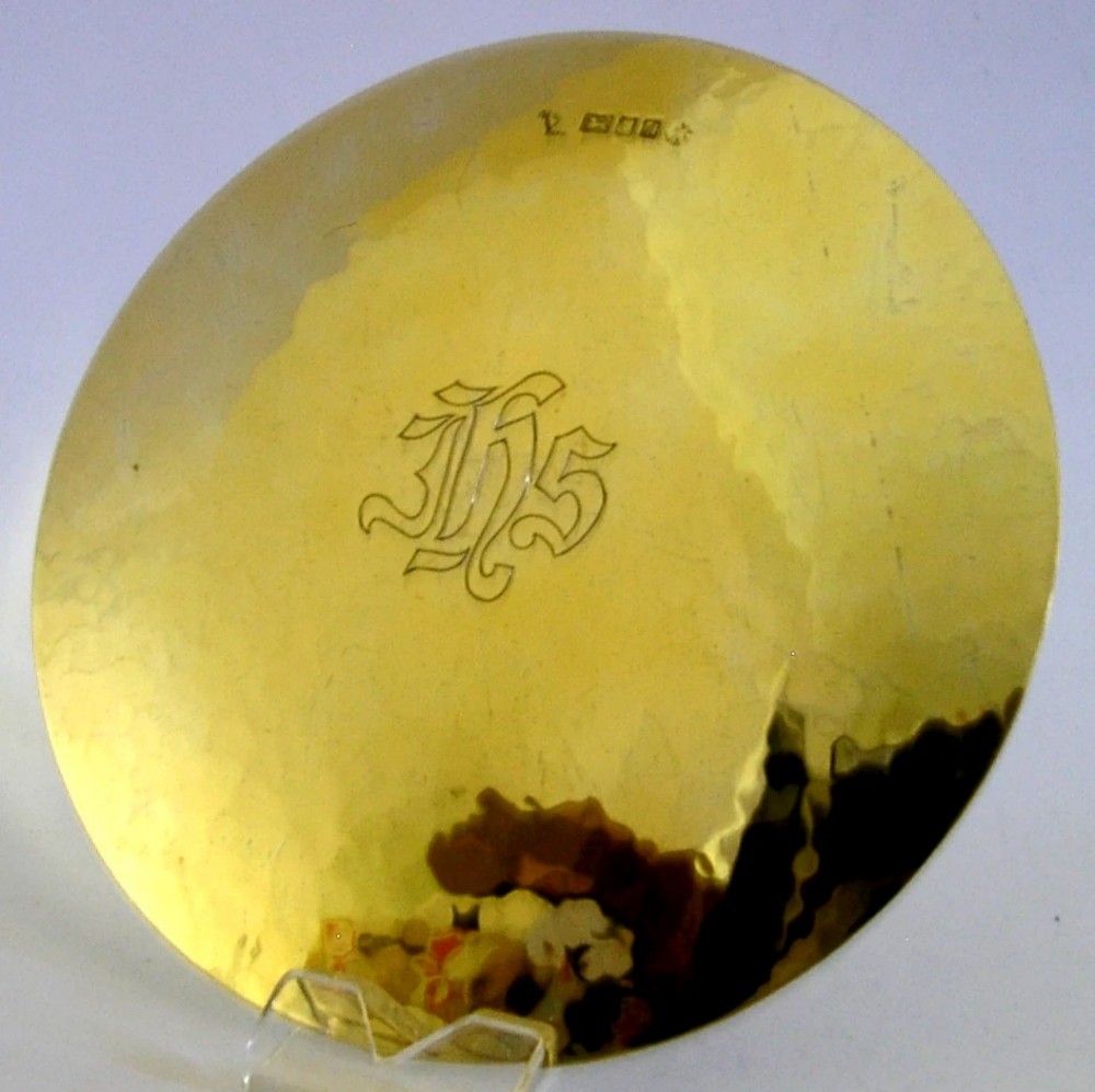 A circular silver gilt paten dish with a hand-hammered finish, featuring an engraved IHS monogram in the centre and hallmarks near the top edge.