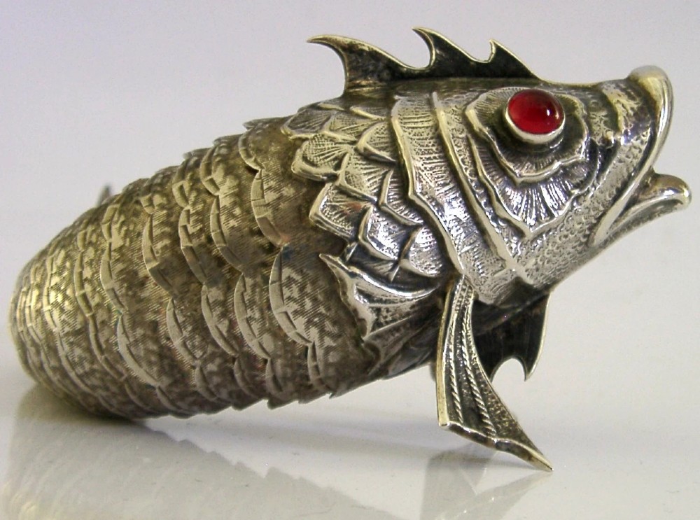 A Spanish silver articulated fish featuring overlapping jointed scales, carved fins, and red cabochon eyes.