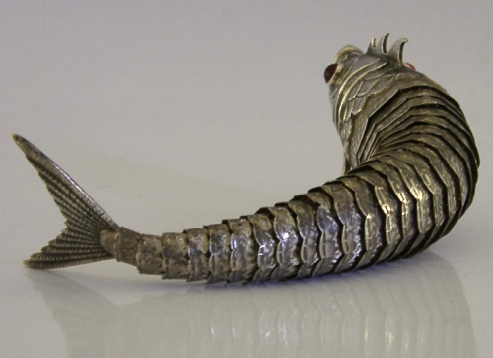 A Spanish silver articulated fish featuring overlapping jointed scales, carved fins, and red cabochon eyes. View V