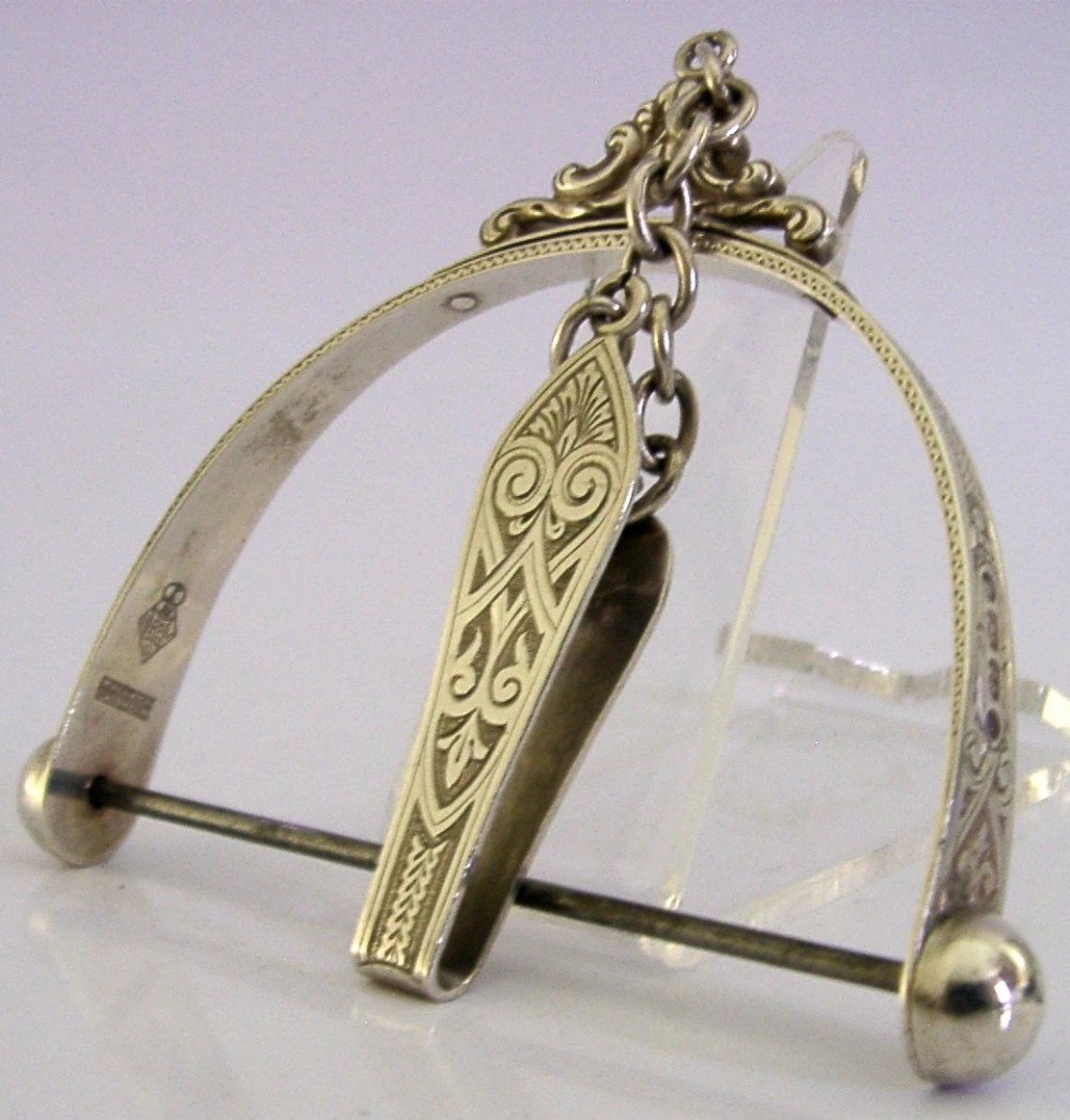 A Victorian sterling silver chatelaine thread spool holder featuring engraved scrollwork motifs and suspension chains.