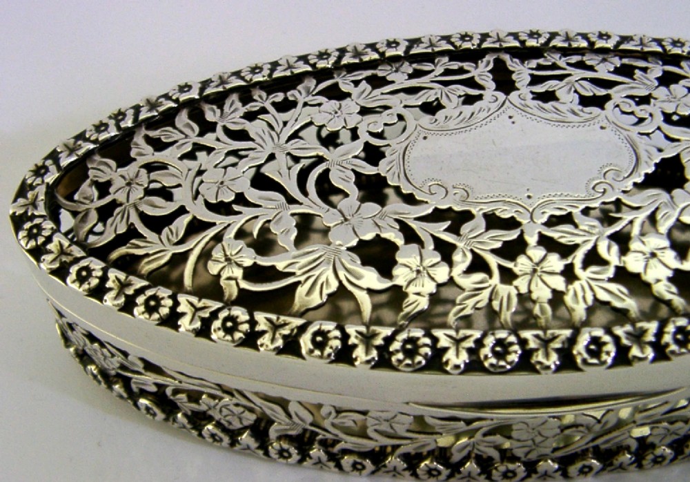 An oval sterling silver box featuring intricate pierced floral decoration, a central blank cartouche, and a gilded interior. View II