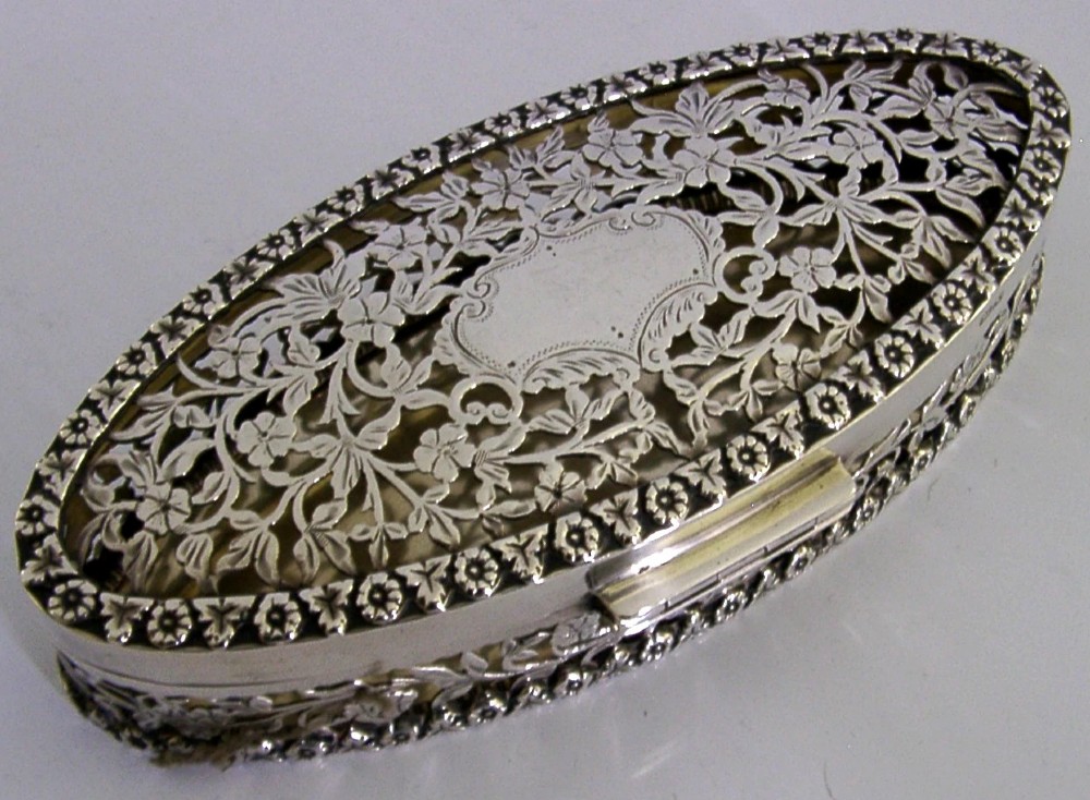 An oval sterling silver box featuring intricate pierced floral decoration, a central blank cartouche, and a gilded interior. View VIII