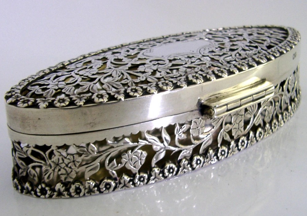 An oval sterling silver box featuring intricate pierced floral decoration, a central blank cartouche, and a gilded interior. View IX