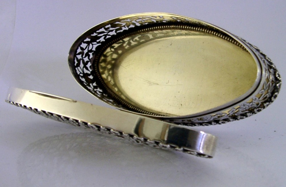 An oval sterling silver box featuring intricate pierced floral decoration, a central blank cartouche, and a gilded interior. View XI