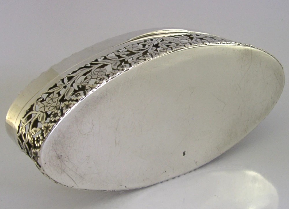 An oval sterling silver box featuring intricate pierced floral decoration, a central blank cartouche, and a gilded interior. View XIII