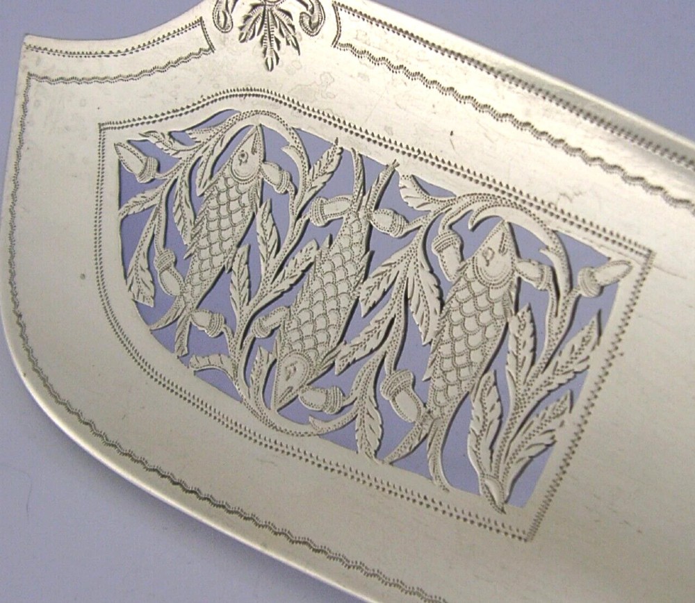 A Victorian sterling silver fish server featuring an intricately engraved blade with foliate patterns and a flat handle. View II