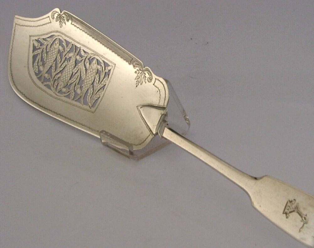 A Victorian sterling silver fish server featuring an intricately engraved blade with foliate patterns and a flat handle. View V