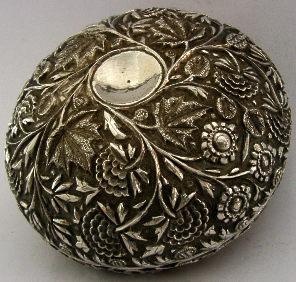 A rounded solid silver bowl featuring detailed repousse floral and foliate hand-chased decoration with a circular central polished medallion.