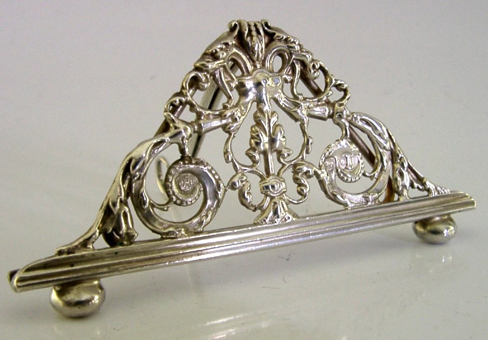 An intricate triangular Victorian sterling silver menu holder featuring pierced scrolling foliage, acanthus leaf motifs, and small ball feet.