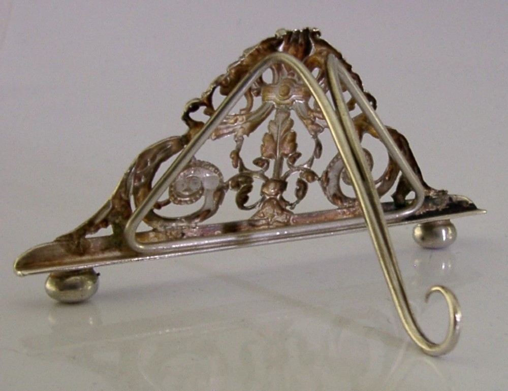 An intricate triangular Victorian sterling silver menu holder featuring pierced scrolling foliage, acanthus leaf motifs, and small ball feet. View II