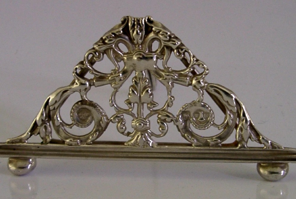 An intricate triangular Victorian sterling silver menu holder featuring pierced scrolling foliage, acanthus leaf motifs, and small ball feet. View III