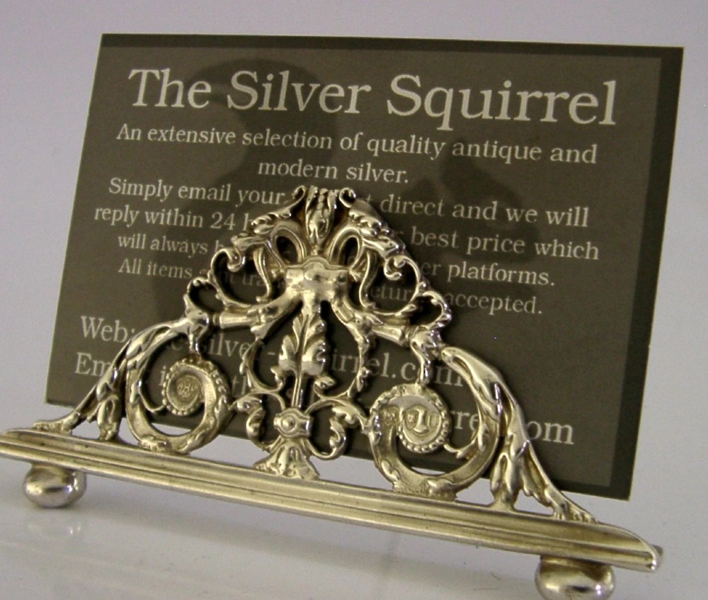 An intricate triangular Victorian sterling silver menu holder featuring pierced scrolling foliage, acanthus leaf motifs, and small ball feet. View IV