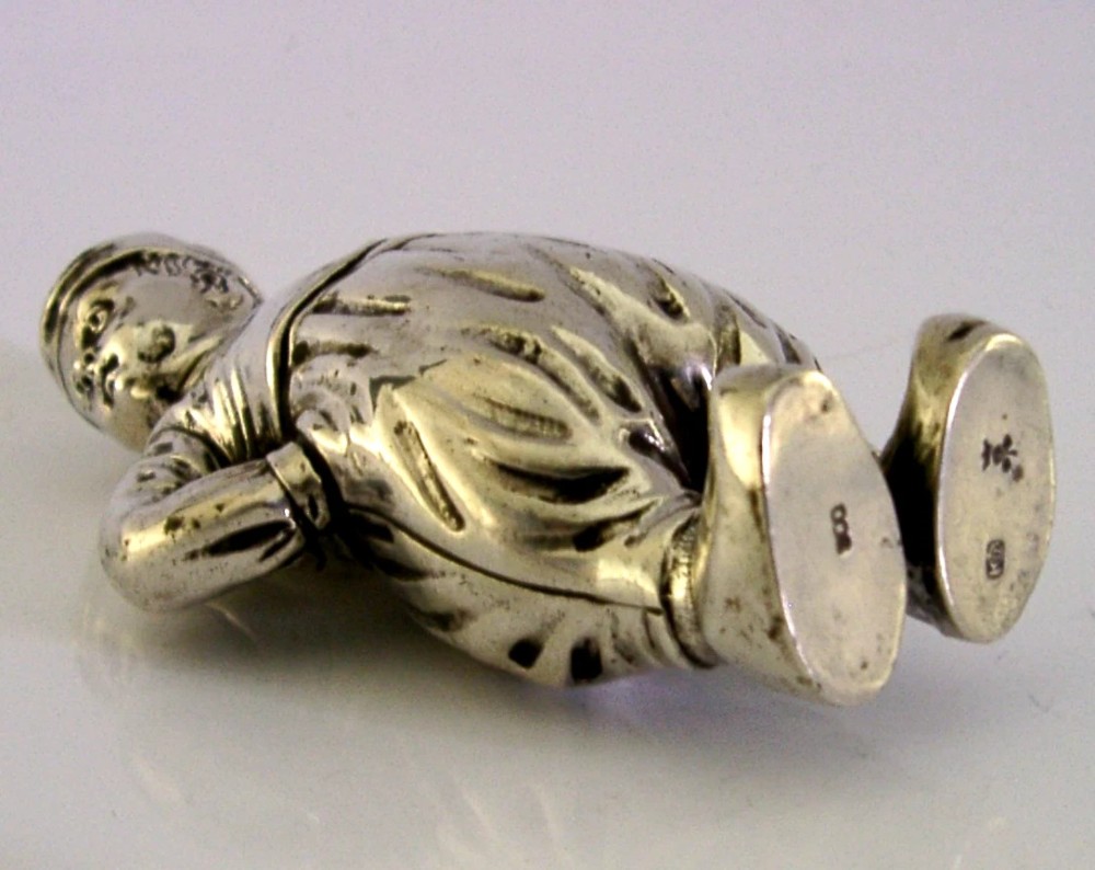 An antique solid silver pepper pot cast in the form of a standing boy wearing a cap, neckscarf, and wide trousers with hands resting on his hips. View VI