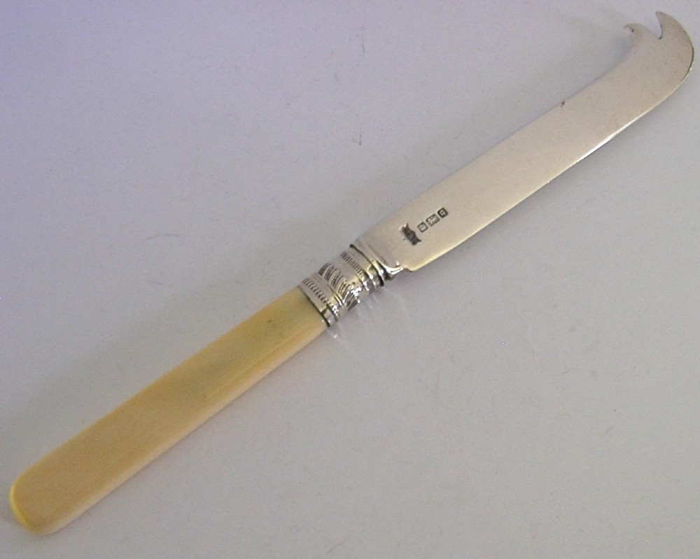 An Edwardian sterling silver cheese knife featuring a smooth cream handle, decorative silver ferrule, and a hallmarked curved silver blade.