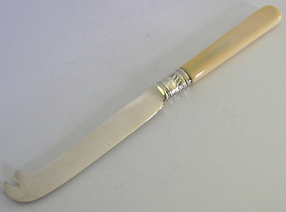 An Edwardian sterling silver cheese knife featuring a smooth cream handle, decorative silver ferrule, and a hallmarked curved silver blade. View II