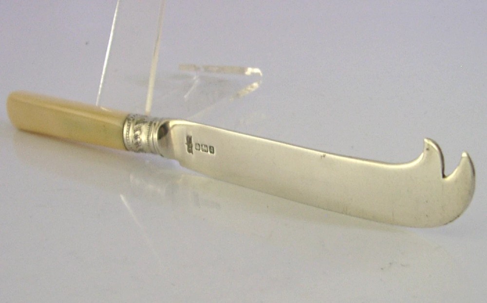 An Edwardian sterling silver cheese knife featuring a smooth cream handle, decorative silver ferrule, and a hallmarked curved silver blade. View III