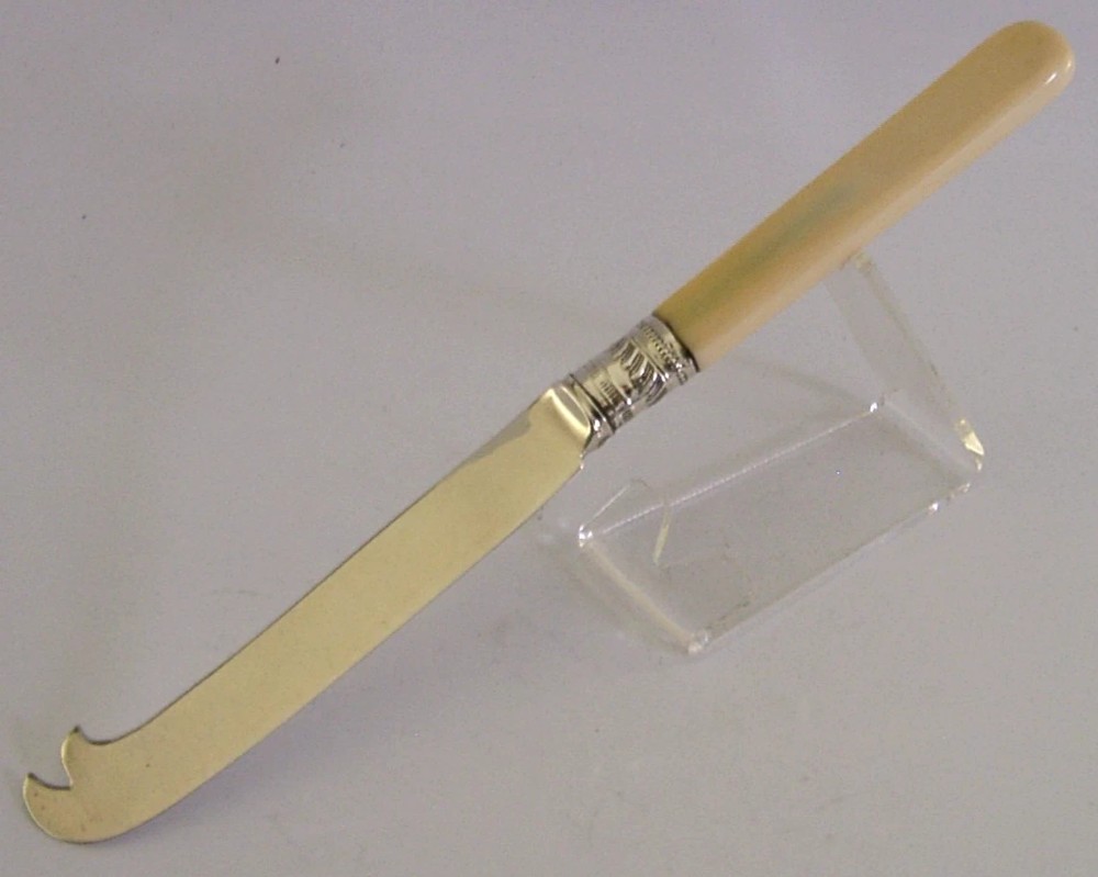 An Edwardian sterling silver cheese knife featuring a smooth cream handle, decorative silver ferrule, and a hallmarked curved silver blade. View IV