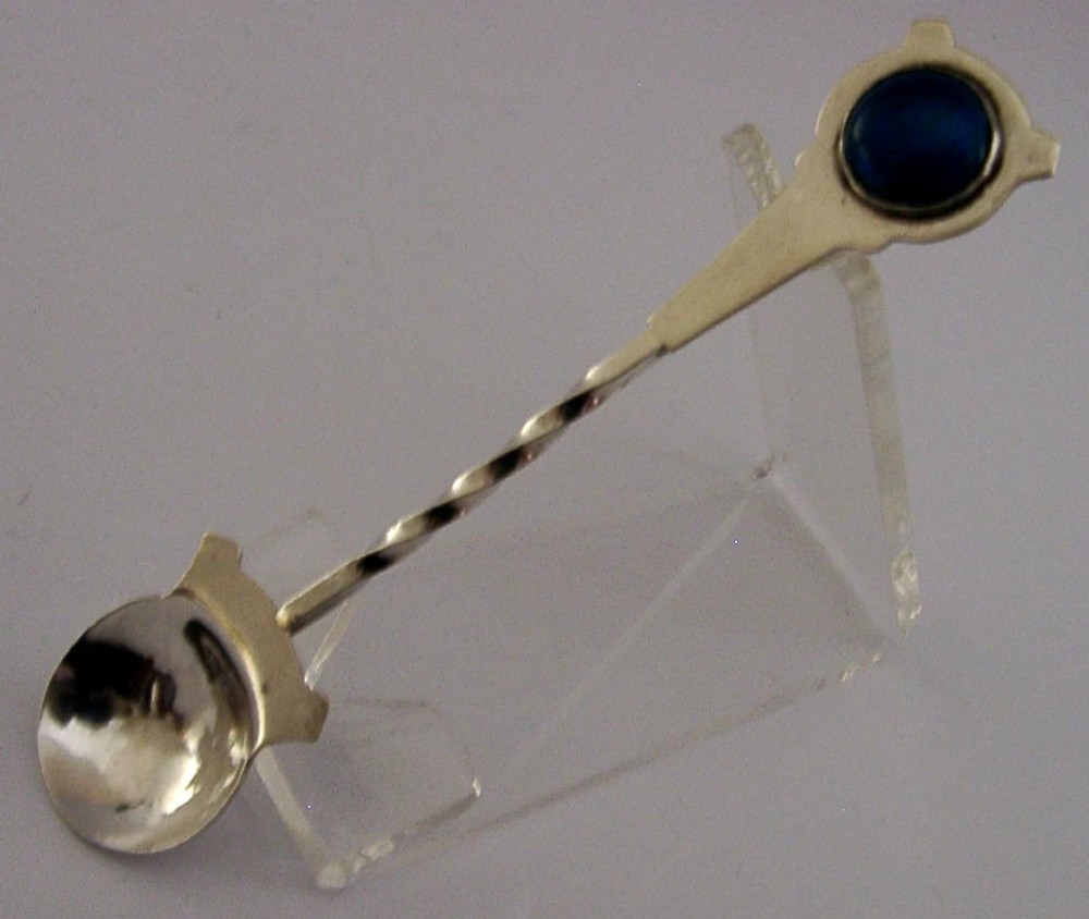 Sterling silver caddy spoon featuring a planished round bowl, a twisted stem, and a circular handle inset with a blue enamel cabochon.