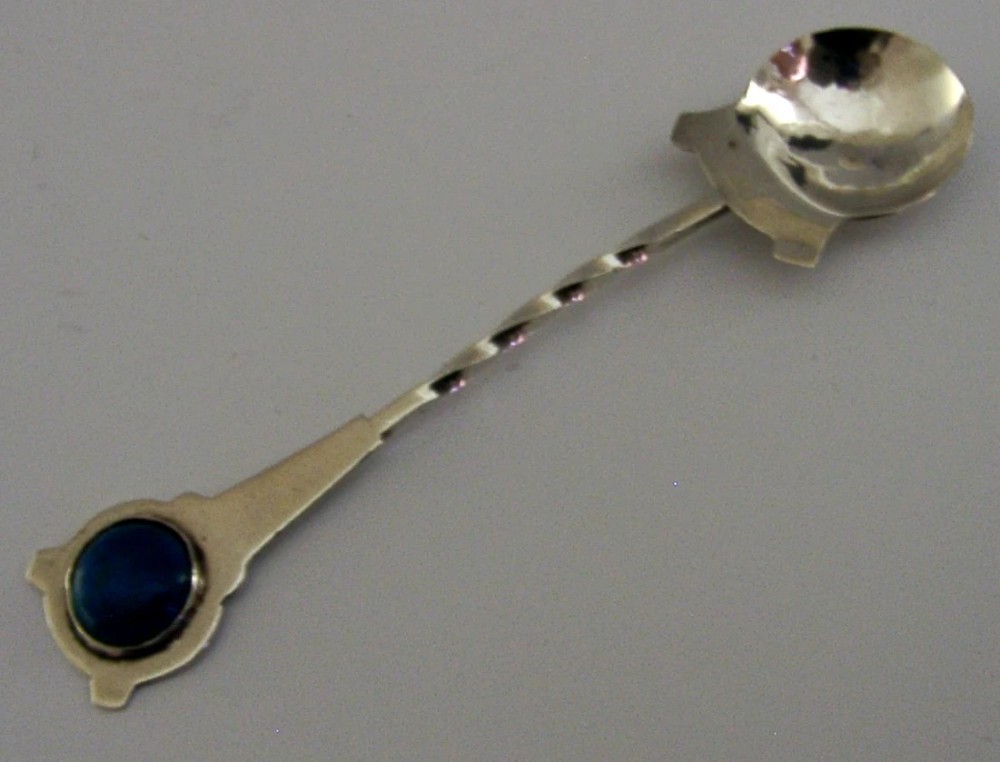 Sterling silver caddy spoon featuring a planished round bowl, a twisted stem, and a circular handle inset with a blue enamel cabochon. View IV