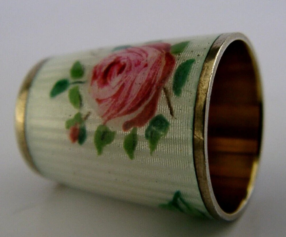 A sterling silver sewing thimble coated in white guilloche enamel featuring a hand-painted pink rose with a textured metal cap. View II