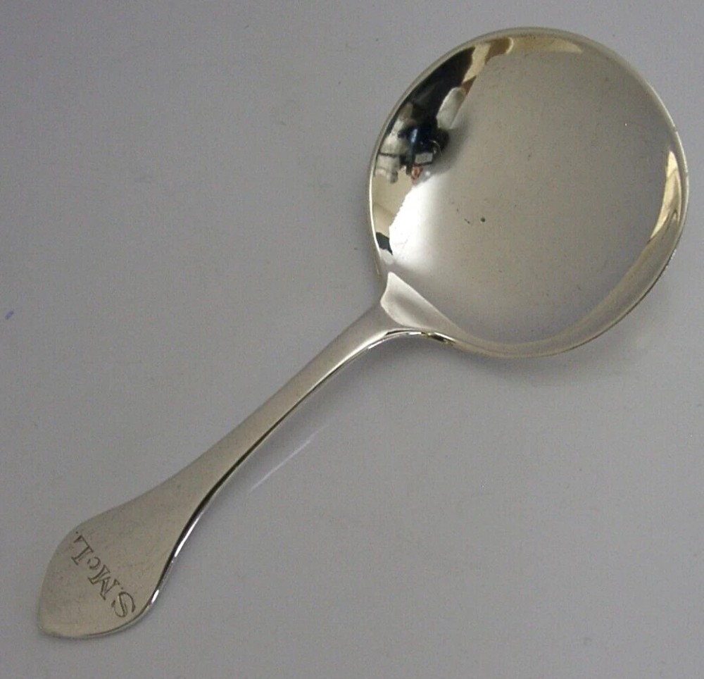An antique sterling silver caddy spoon featuring a rounded shallow bowl and a tapered handle with engraved initials.