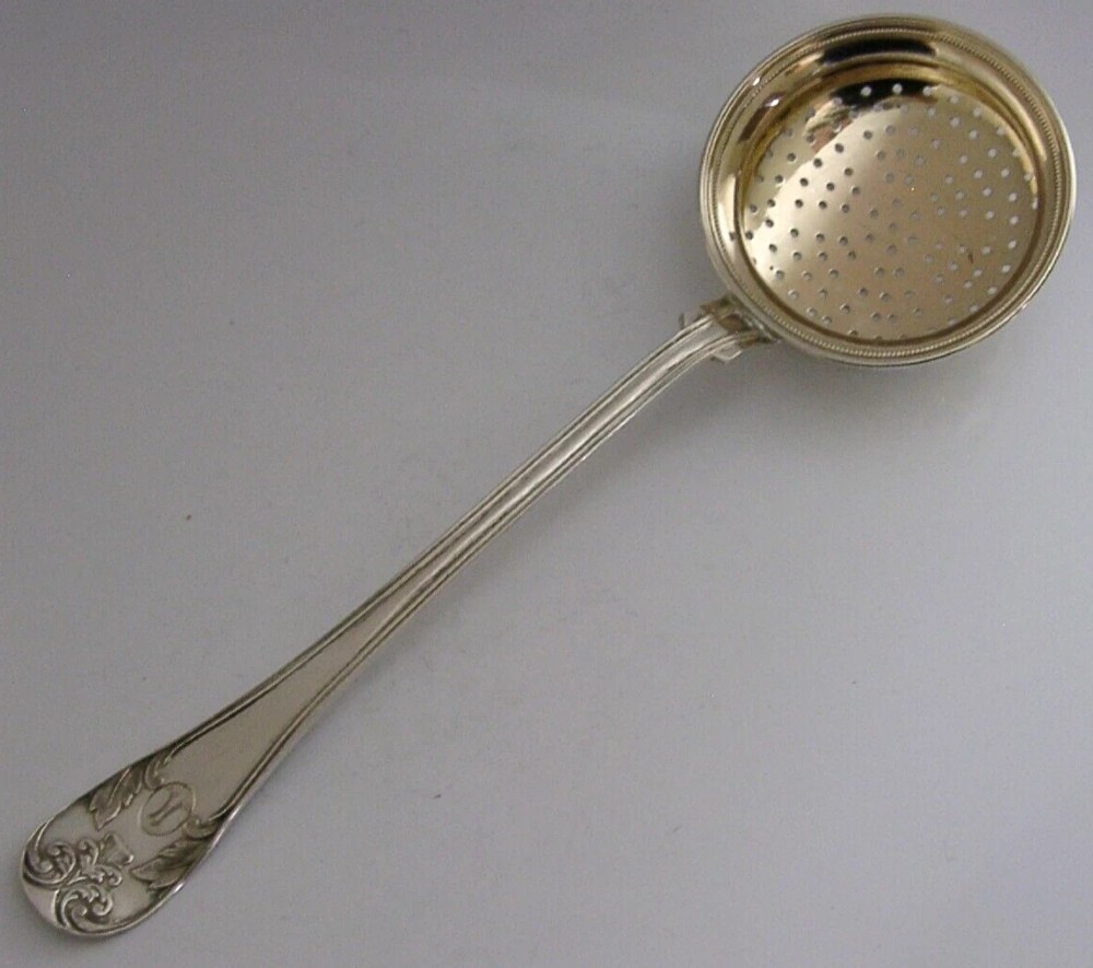 An antique solid silver sugar sifter spoon featuring a round perforated bowl and an engraved foliate handle dated 1903.