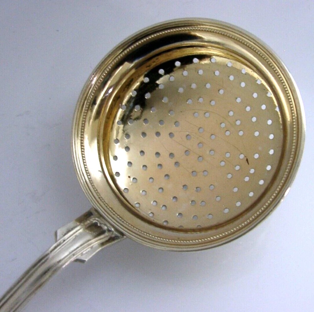 An antique solid silver sugar sifter spoon featuring a round perforated bowl and an engraved foliate handle dated 1903. View II