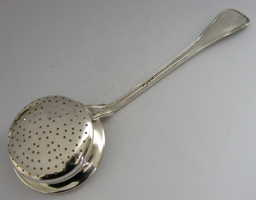 An antique solid silver sugar sifter spoon featuring a round perforated bowl and an engraved foliate handle dated 1903. View IV