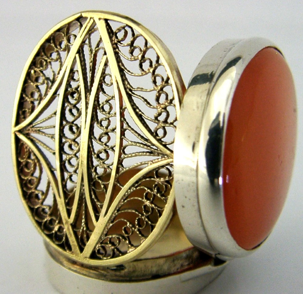 An oval Georgian sterling silver vinaigrette box shown open to reveal an orange agate inset lid and an articulated filigree inner grille. View II