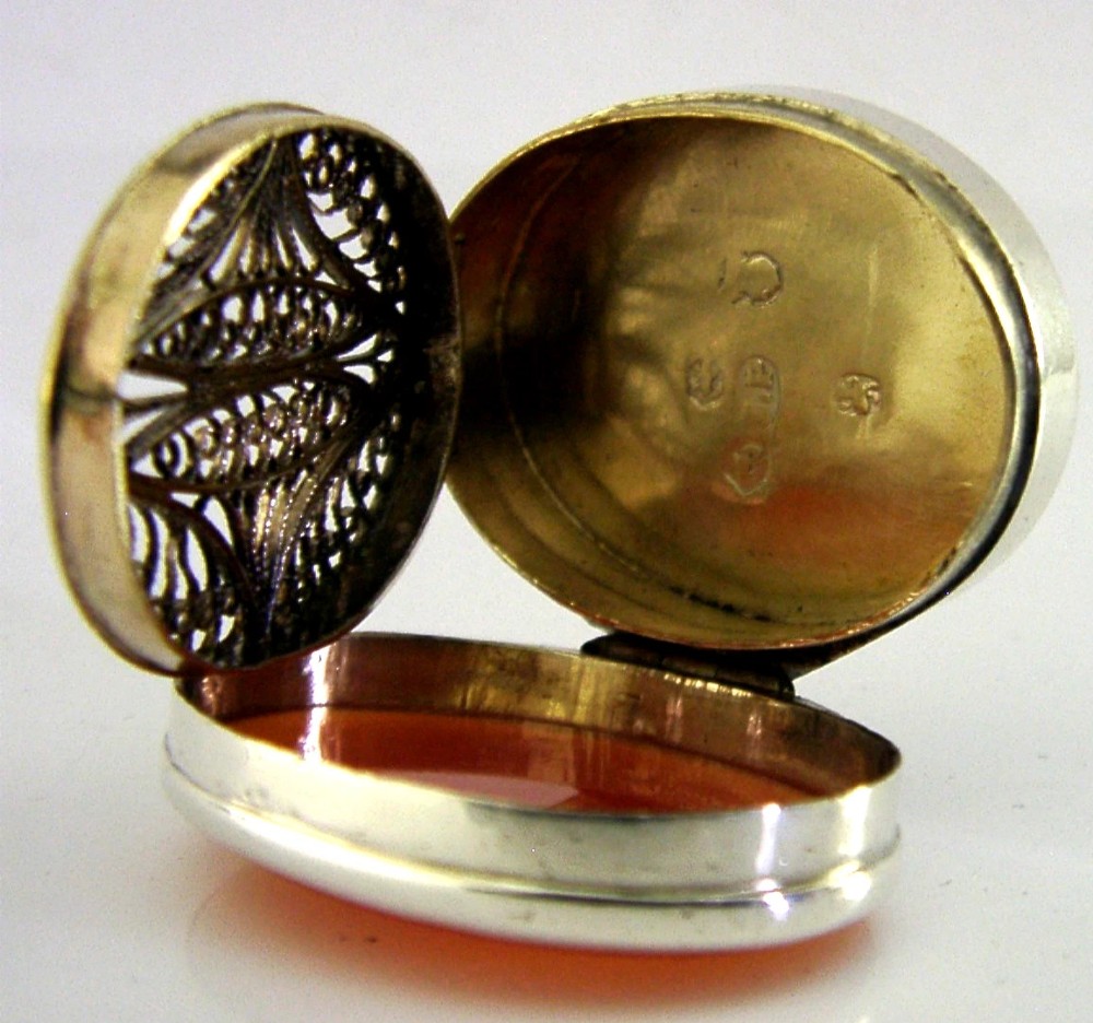 An oval Georgian sterling silver vinaigrette box shown open to reveal an orange agate inset lid and an articulated filigree inner grille. View VI
