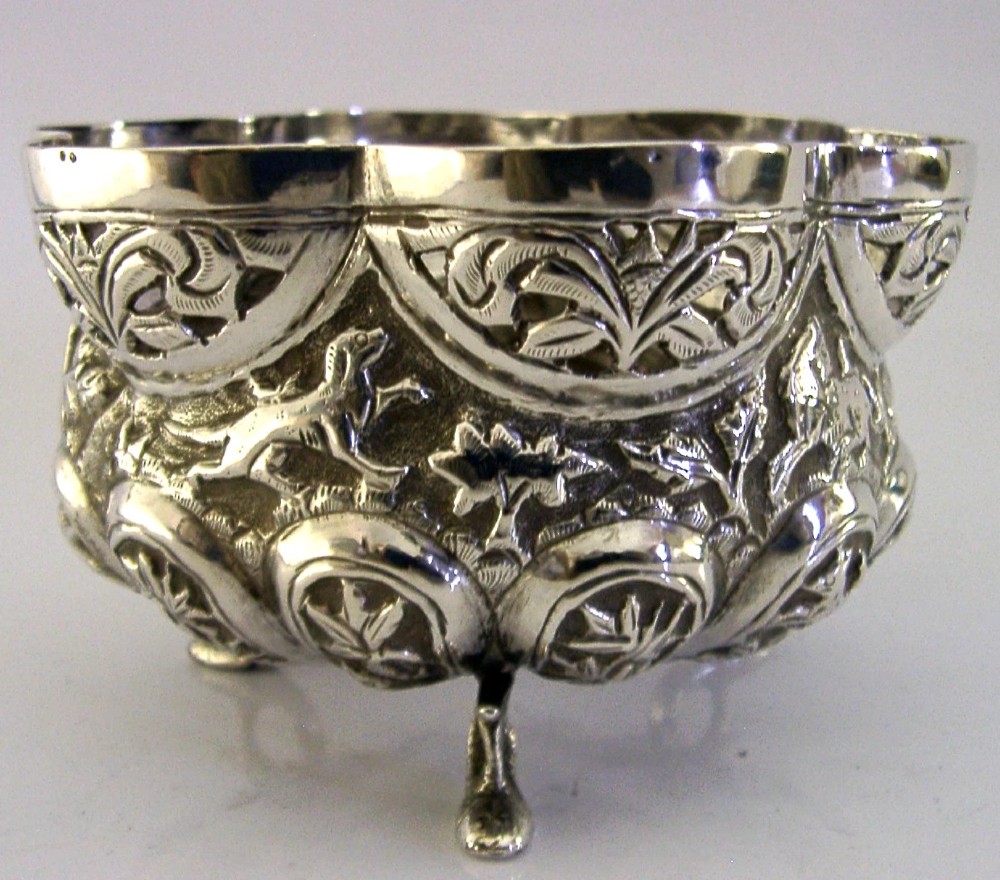 A small footed solid silver bowl featuring intricate repousse floral and animal motifs with a scalloped rim.
