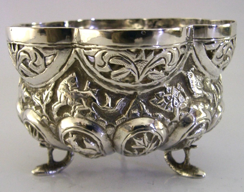 A small footed solid silver bowl featuring intricate repousse floral and animal motifs with a scalloped rim. View IV