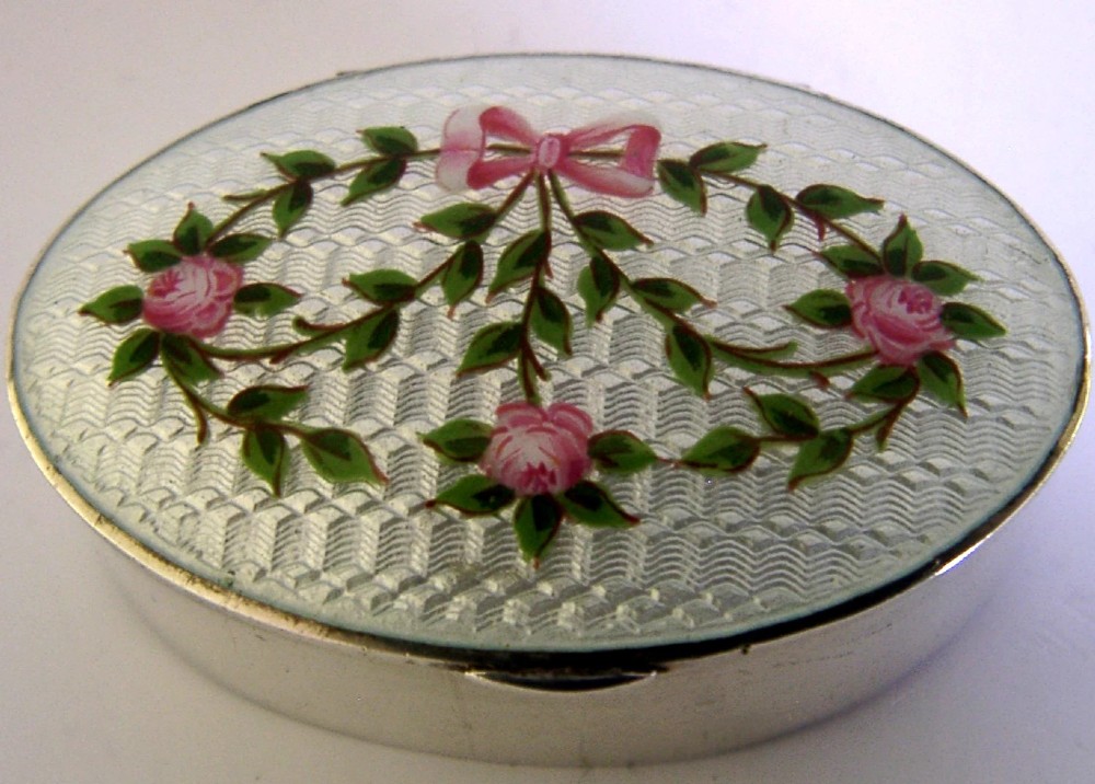 An oval sterling silver trinket box featuring a light blue guilloche enamel lid detailed with hand-painted pink roses and a ribbon garland.