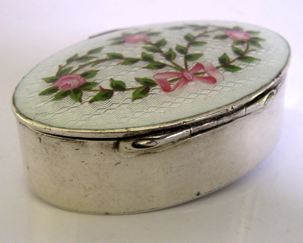 An oval sterling silver trinket box featuring a light blue guilloche enamel lid detailed with hand-painted pink roses and a ribbon garland. View V