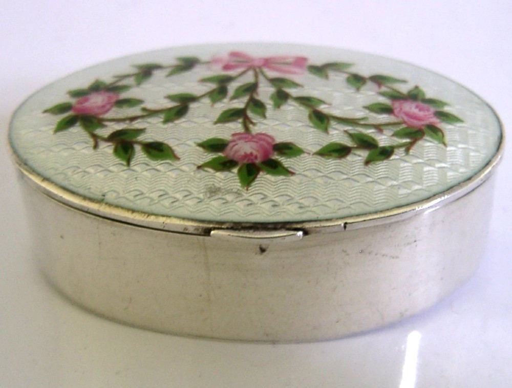 An oval sterling silver trinket box featuring a light blue guilloche enamel lid detailed with hand-painted pink roses and a ribbon garland. View VI