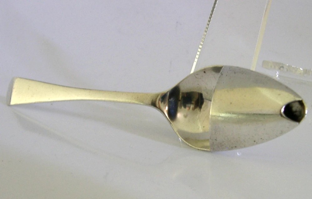 An antique sterling silver medicine spoon featuring a tapered handle and a partially covered bowl with a pouring spout.