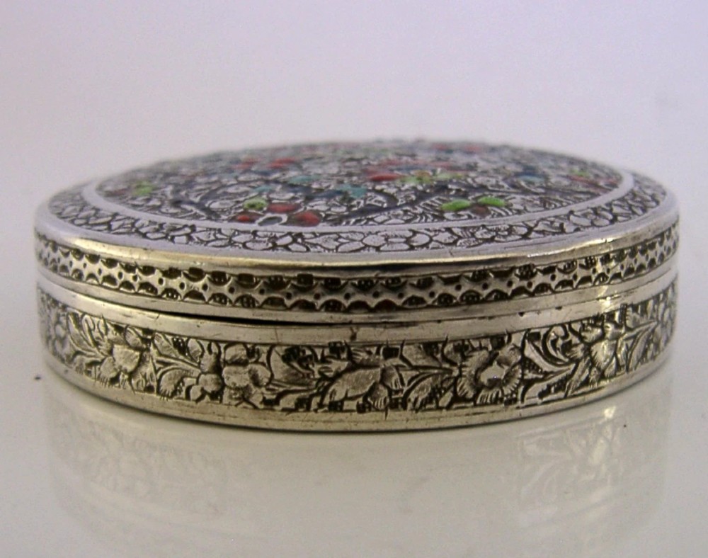 A circular solid silver trinket box with a hinged lid decorated with chased metalwork and polychrome floral enamelling in red, green, and blue. View II