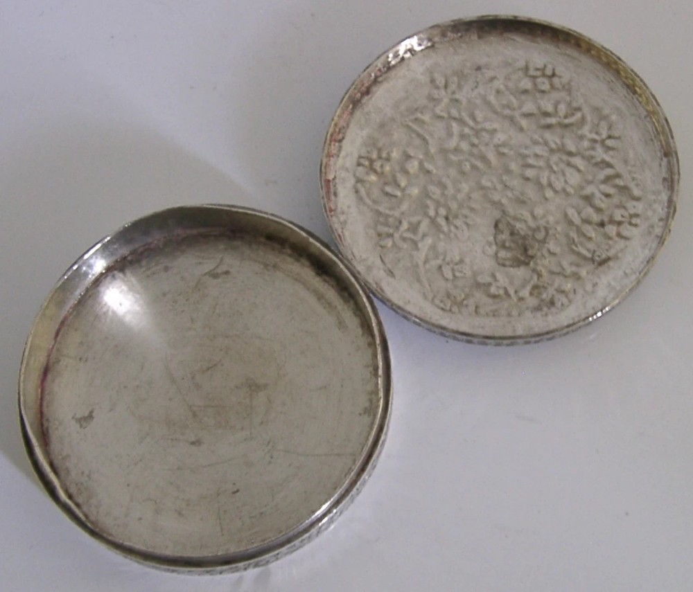 A circular solid silver trinket box with a hinged lid decorated with chased metalwork and polychrome floral enamelling in red, green, and blue. View III