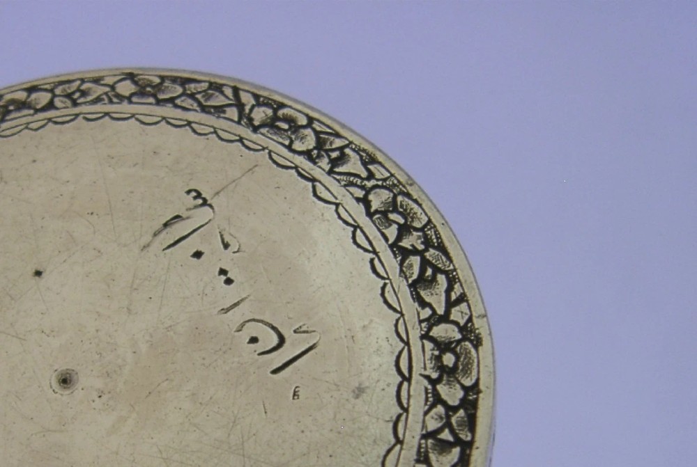 A circular solid silver trinket box with a hinged lid decorated with chased metalwork and polychrome floral enamelling in red, green, and blue. View V