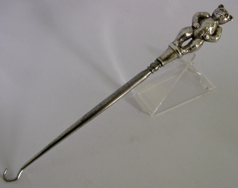 An Edwardian sterling silver button hook featuring a figurative teddy bear handle connected to a long steel shaft.