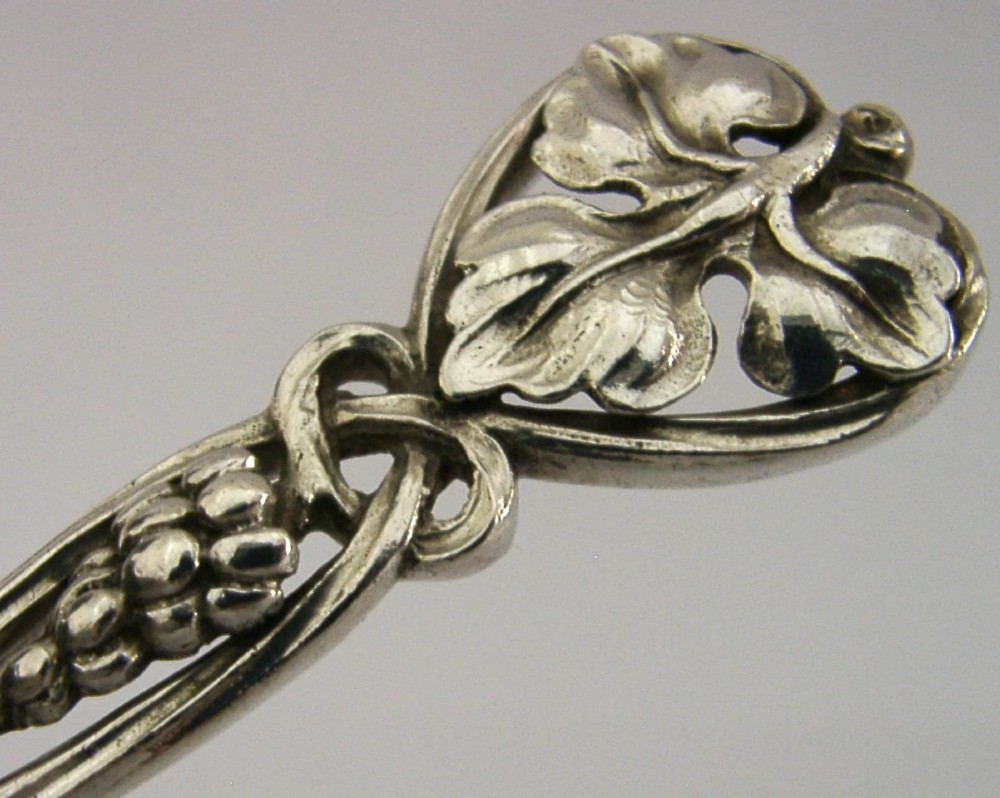 A sterling silver pastry server with a rounded flat spade blade and an openwork handle decorated with carved leaf and grape cluster motifs. View II