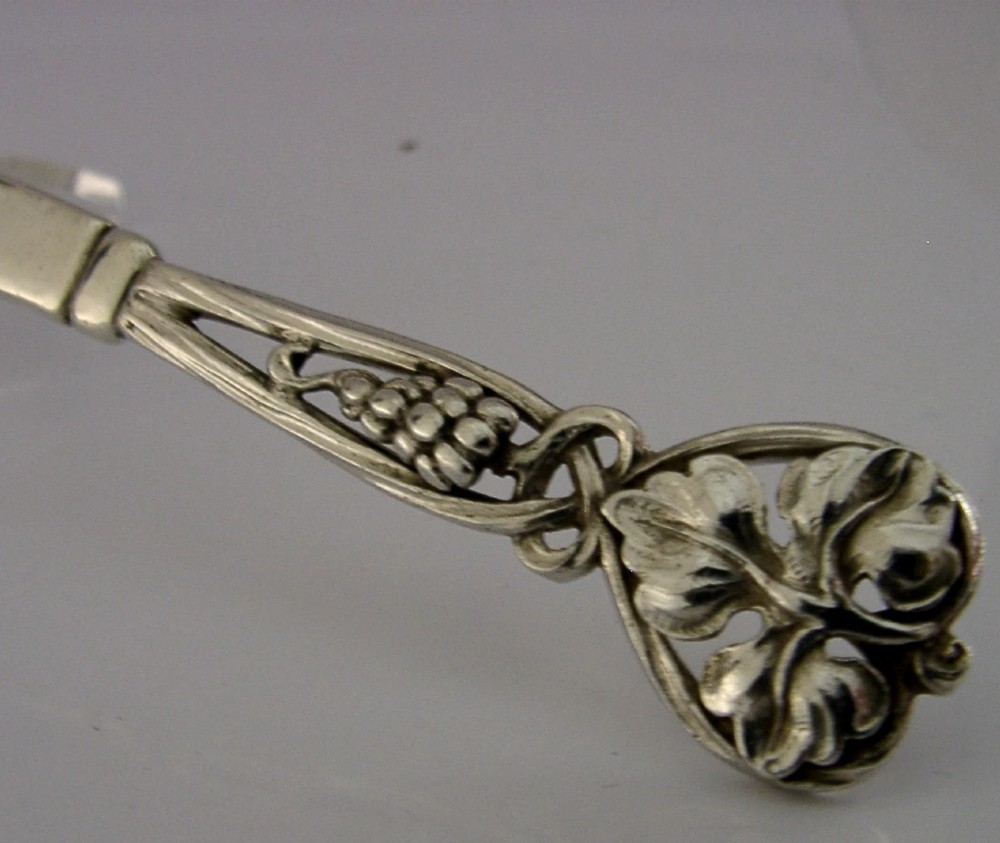 A sterling silver pastry server with a rounded flat spade blade and an openwork handle decorated with carved leaf and grape cluster motifs. View III