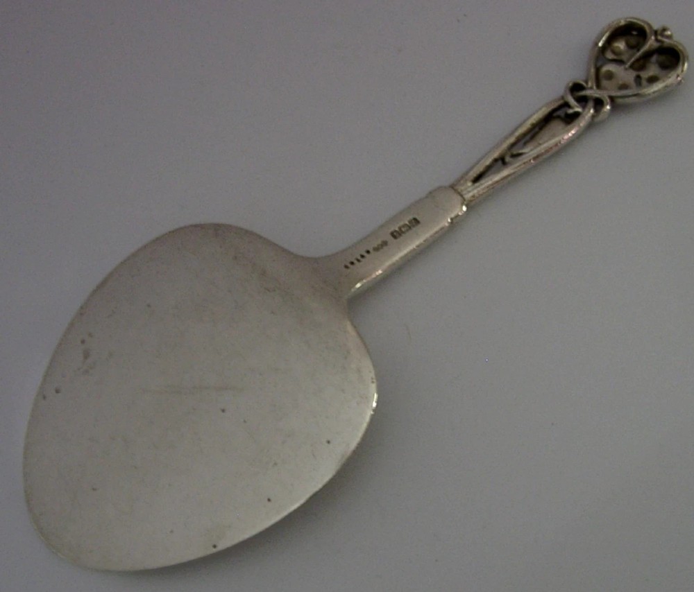 A sterling silver pastry server with a rounded flat spade blade and an openwork handle decorated with carved leaf and grape cluster motifs. View VI